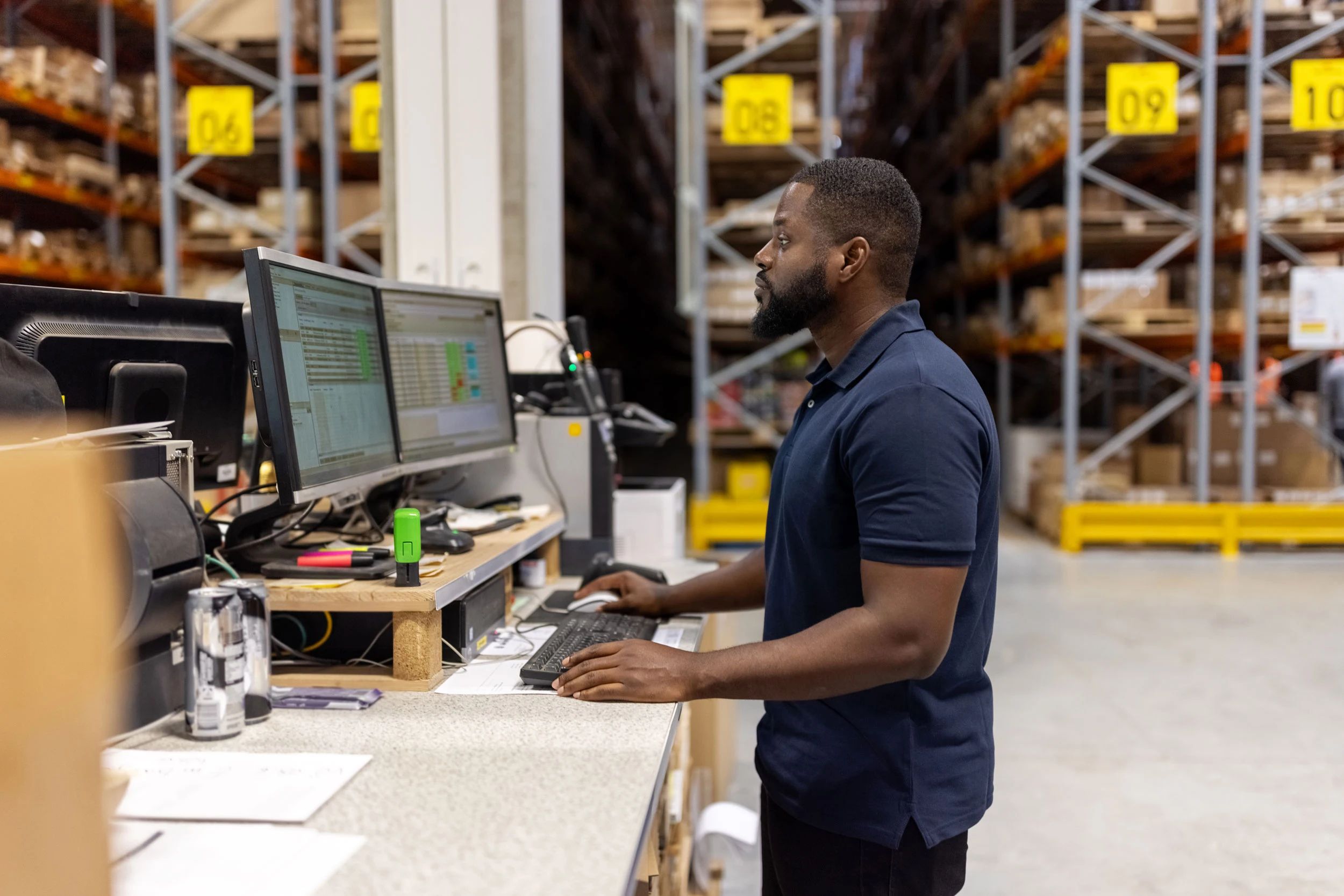 Warehouse operator working at a dual-monitor workstation on the floor