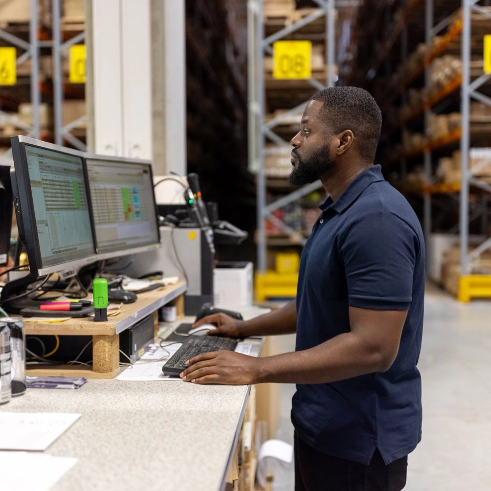 Warehouse operator working at a dual-monitor workstation on the floor