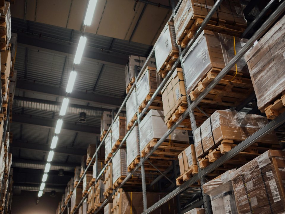 Looking up a tall warehouse aisle between rows of loaded pallet racking, lit by ceiling skylights
